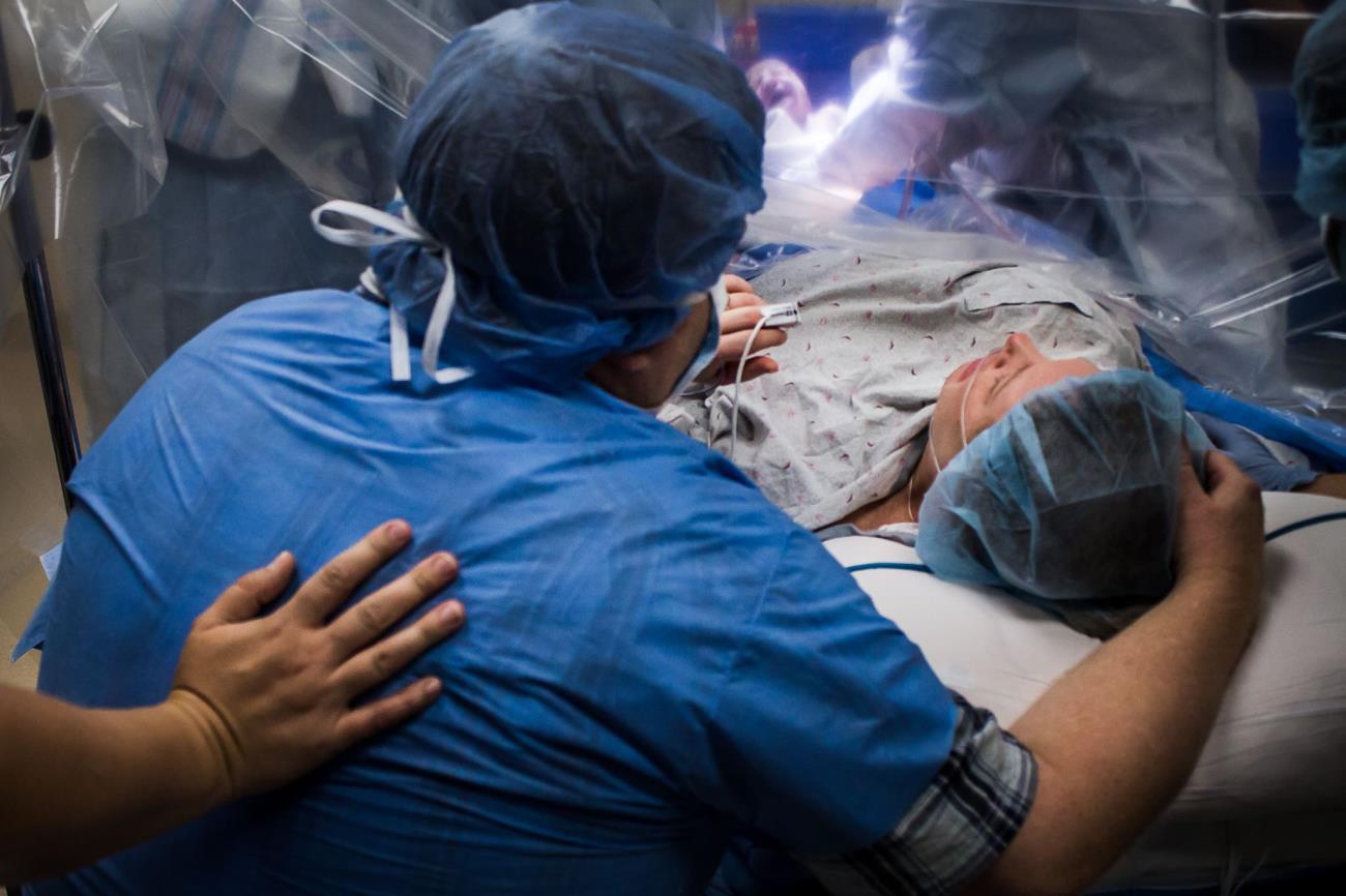 A cesarean section is completed successfully as the mother is comforted by her partner and a birth doula continues to provide emotional support