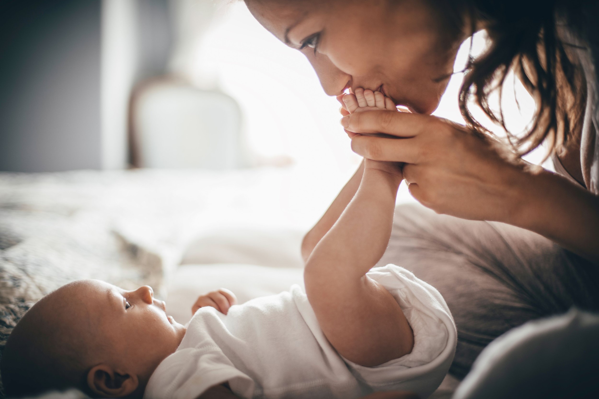 A mother kissing her babies toes as the baby stares happily at her