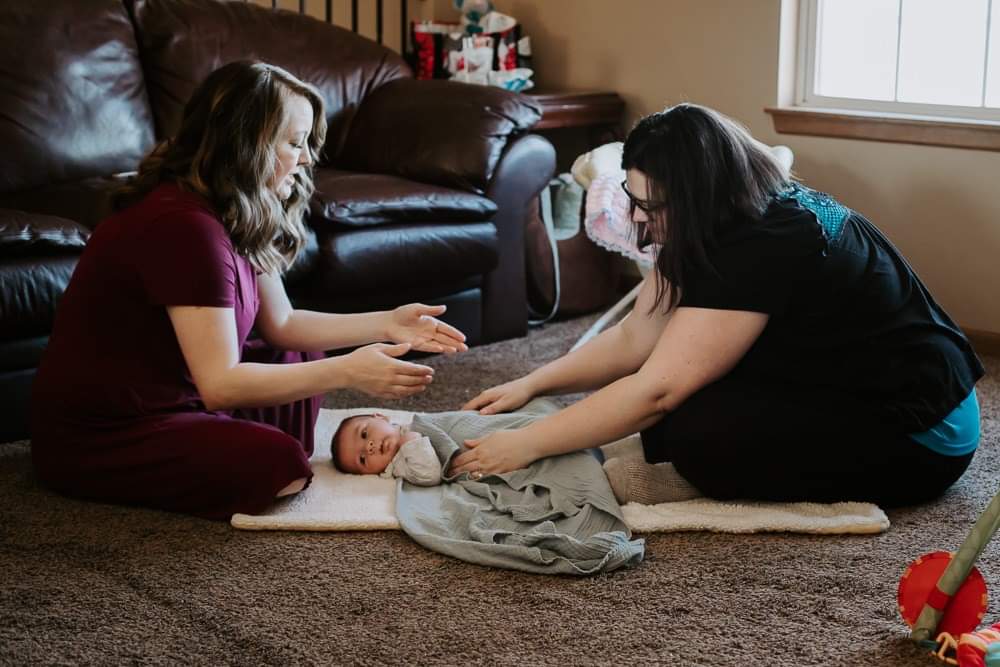 A mother learning different swaddling techniques from a postpartum doula